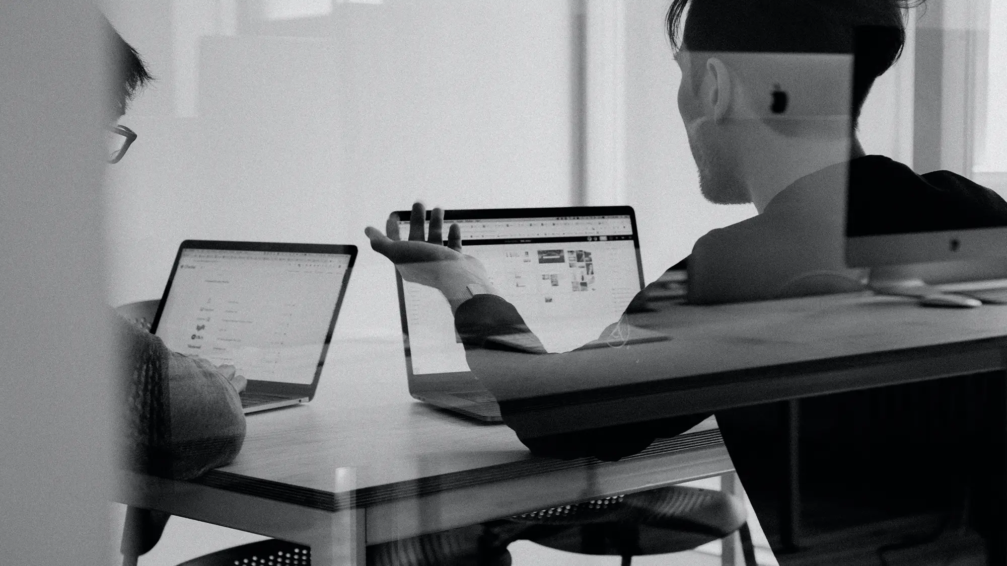 Two colleagues collaborating at laptops in an office, black and white