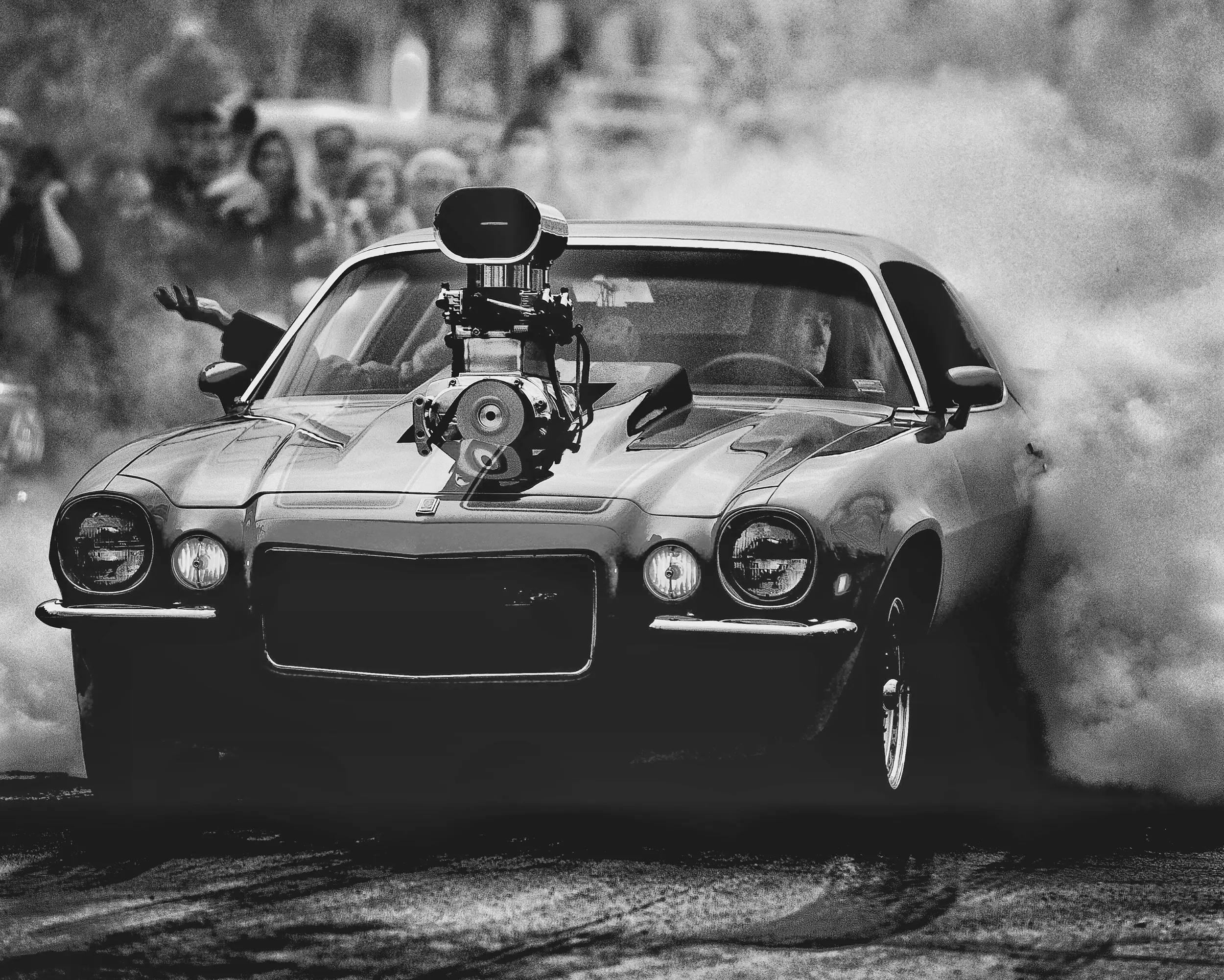 A muscle car performing a smoky burnout in front of a crowd, black and white