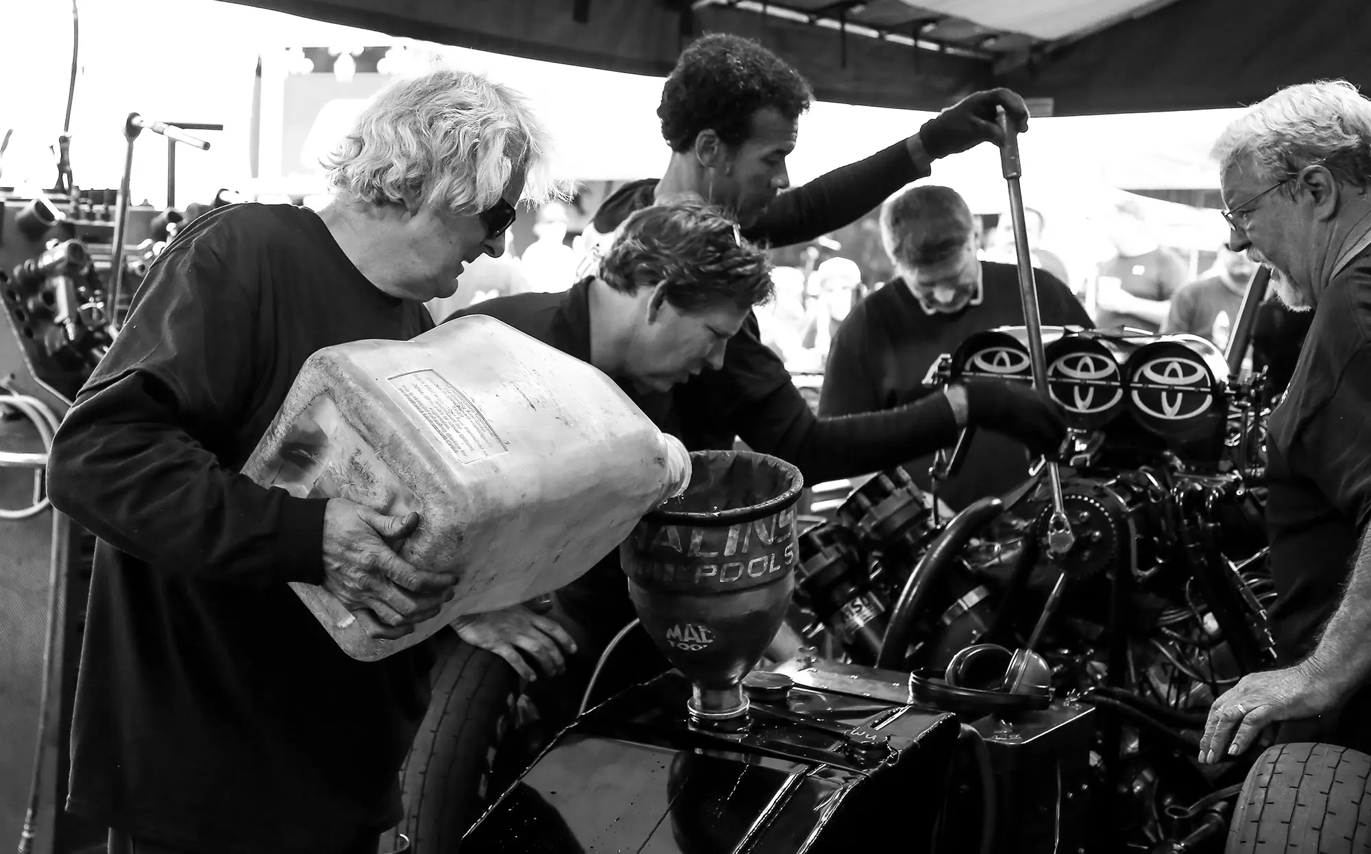 A racing pit crew working on a race car engine, black and white