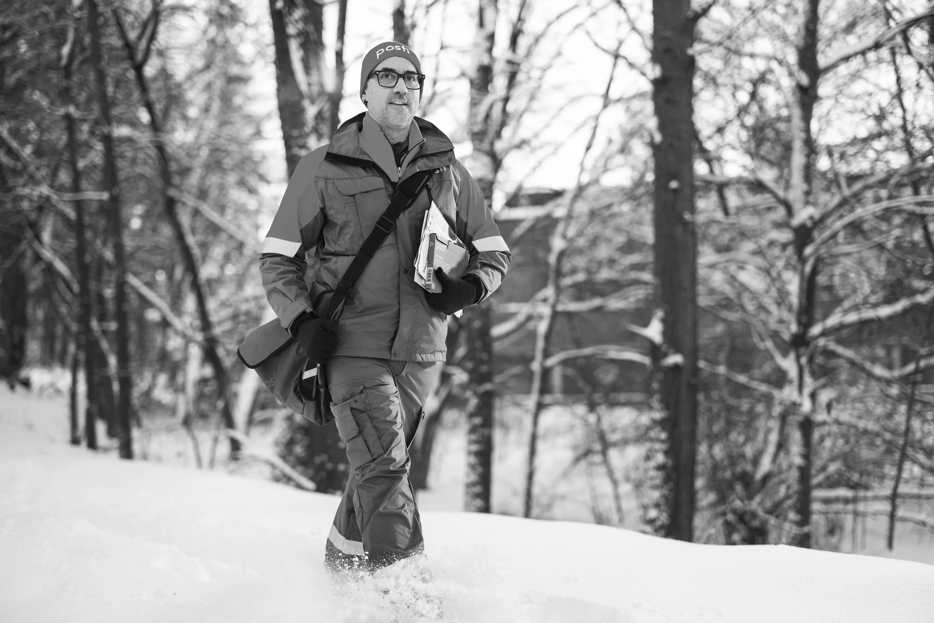 A postal carrier delivering mail on foot through a snowy forest, black and white
