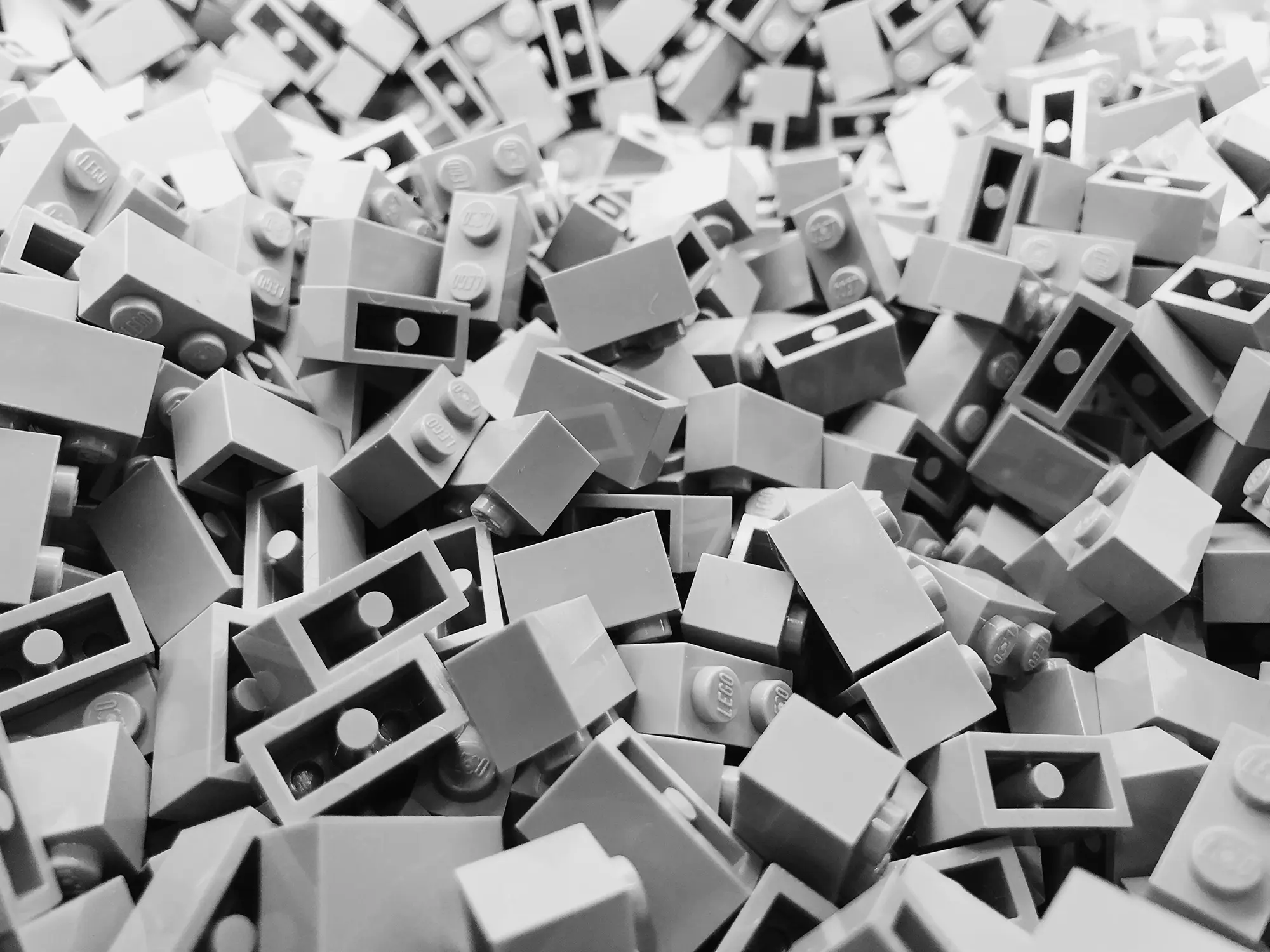A large pile of identical grey Lego building bricks, monochrome