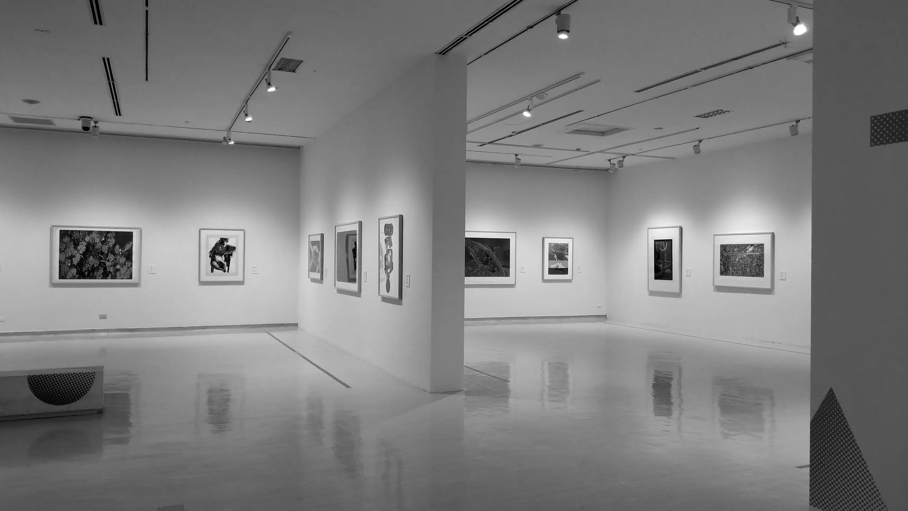 A bright gallery interior with framed artworks on white walls and a polished floor, black and white