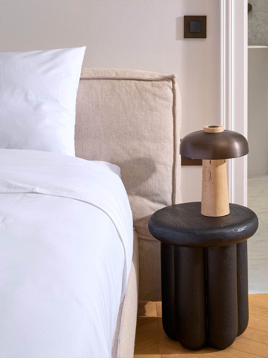 Nightstand detail with a handcrafted designer table and sculptural lamp, enhancing a refined bedroom setting.
