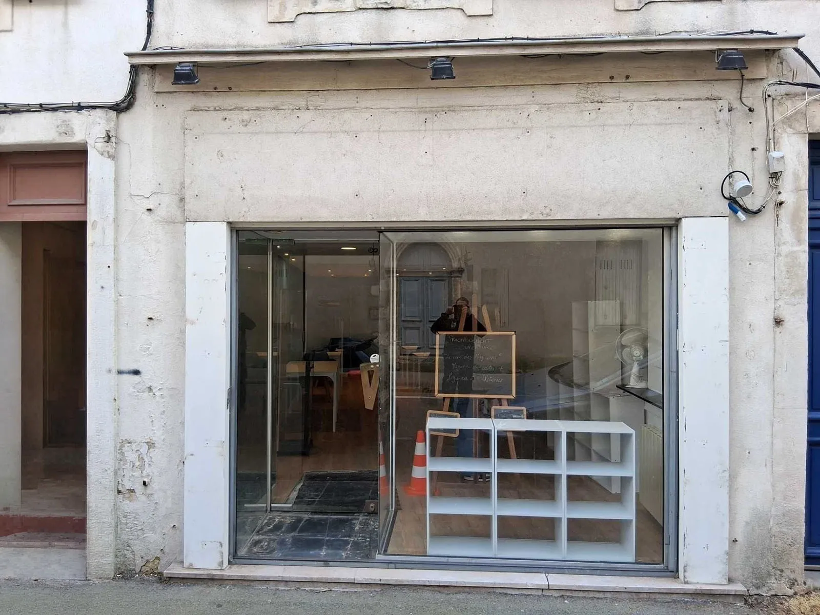 Façade d'un local commercial vide avec une grande vitrine, un meuble blanc et un panneau noir.