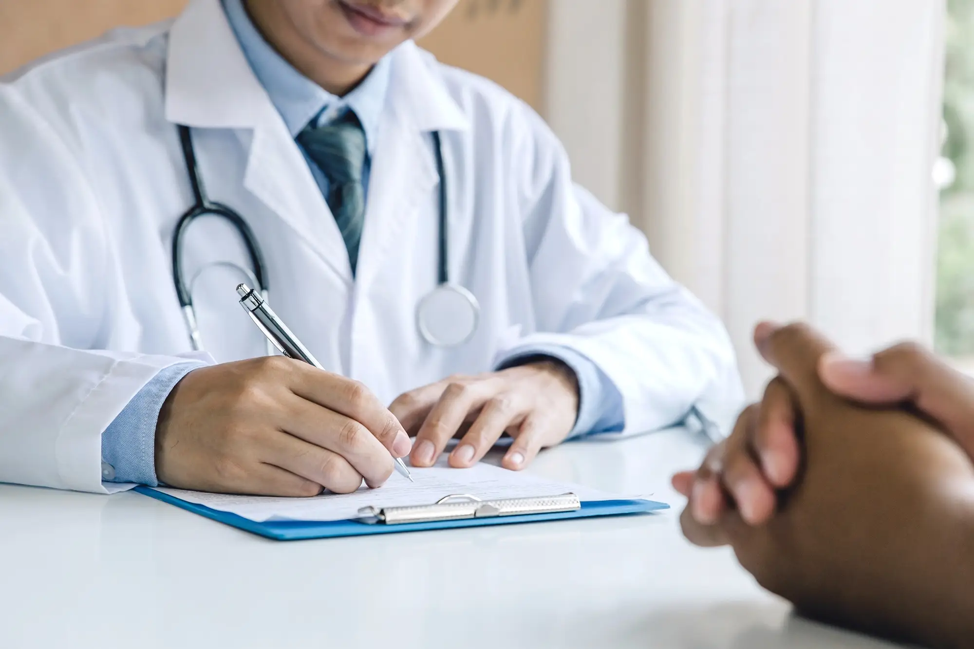 PRP Therapie Kosten: Im Gespräch mit der behandelten Person dokumentiert ein Arzt die Behandlung auf einem Klemmbrett.