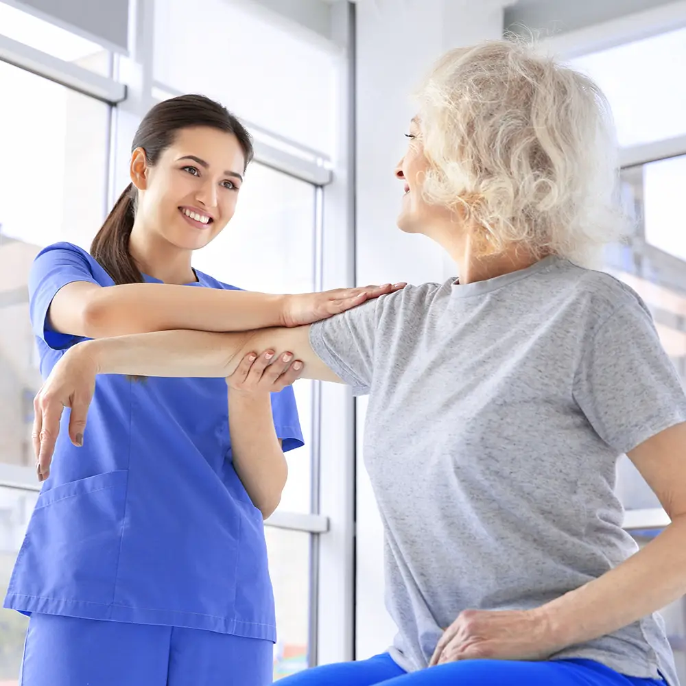 PRP Therapie bei Arthrose: Eine Ärztin hilft einer älteren Patientin bei einer Übung mit dem Oberarm bzw. Schultergelenk.