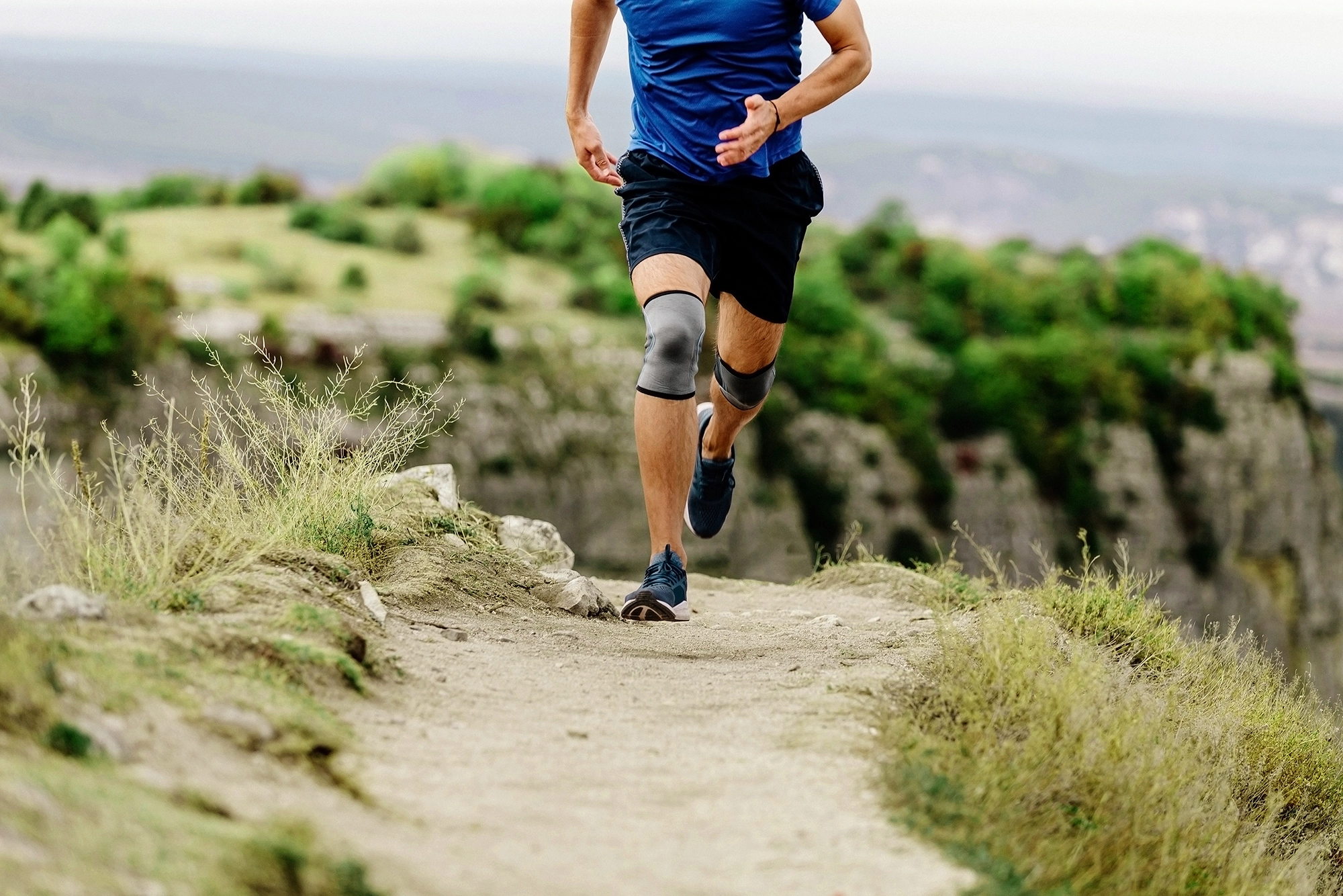 Mann joggt auf auf einem Naturpfad mit Knieschiene und ist wieder aktiv nach einer Eigenbluttherapie.