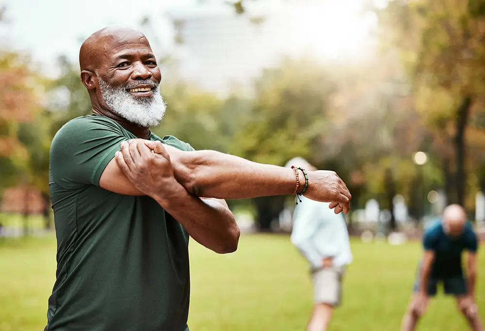 Älterer Mann bei einer sportlichen Dehnübung im Park zur Unterstützung der Regeneration nach Eigenbluttherapie.