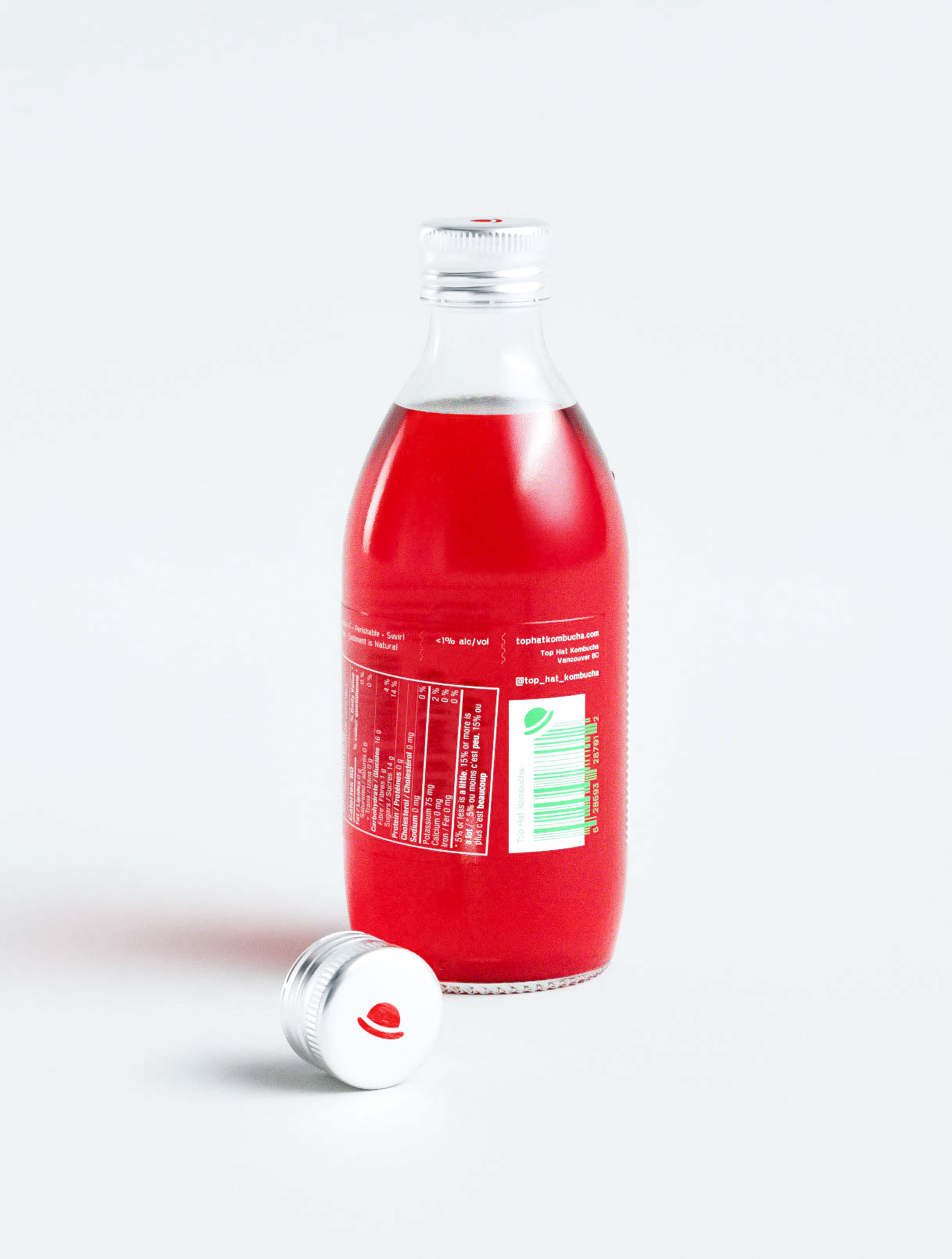 Minimalist kombucha packaging design featuring vibrant red fermented beverage in classic glass bottle with strategic label placement and nutrition panel integration. Professional design studio execution showcasing clean typography hierarchy with barcode placement and social media handle incorporation. Creative branding agency portfolio demonstrating expertise in probiotic beverage packaging with aluminum screw cap detail and transparent product visibility for health-conscious market positioning.