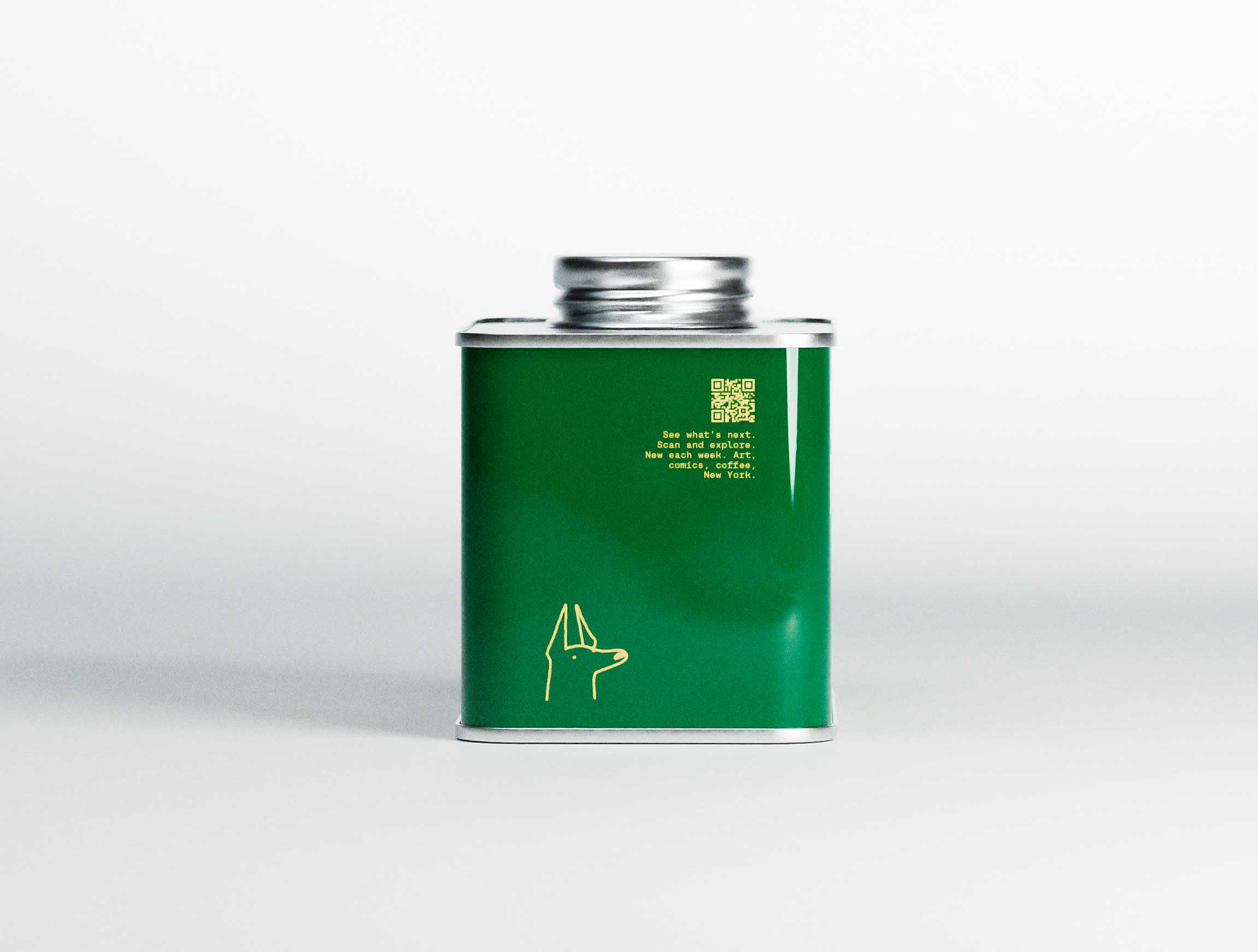 Back view of the deep green Earnest Pursuit coffee tin photographed against a soft light grey studio background. A small QR code and concise typographic message sit centered near the top, while a minimal gold line illustration of a Doberman appears near the base. The matte label contrasts with the reflective silver lid and frame, highlighted by controlled natural lighting. The restrained composition demonstrates packaging design studio discipline, where branding, hierarchy, and negative space are carefully balanced within a contemporary graphic design system.