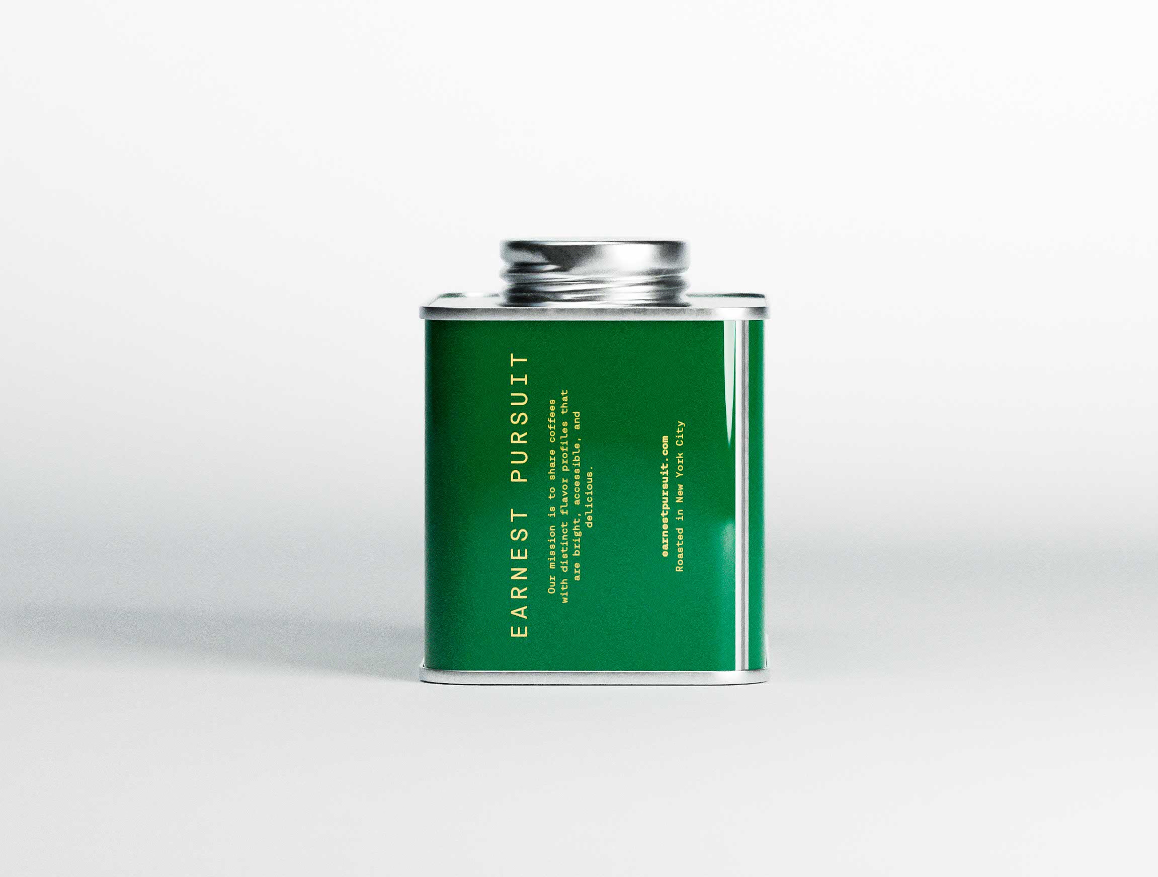 Side profile of the green Earnest Pursuit coffee tin set against a clean light backdrop. Vertical gold typography spells the brand name along the panel edge, accompanied by concise mission text and roasting details. The metallic lid catches subtle highlights, reinforcing material quality. The composition showcases branding studio precision and confident creative direction, where typographic alignment and margin control define the packaging design architecture.