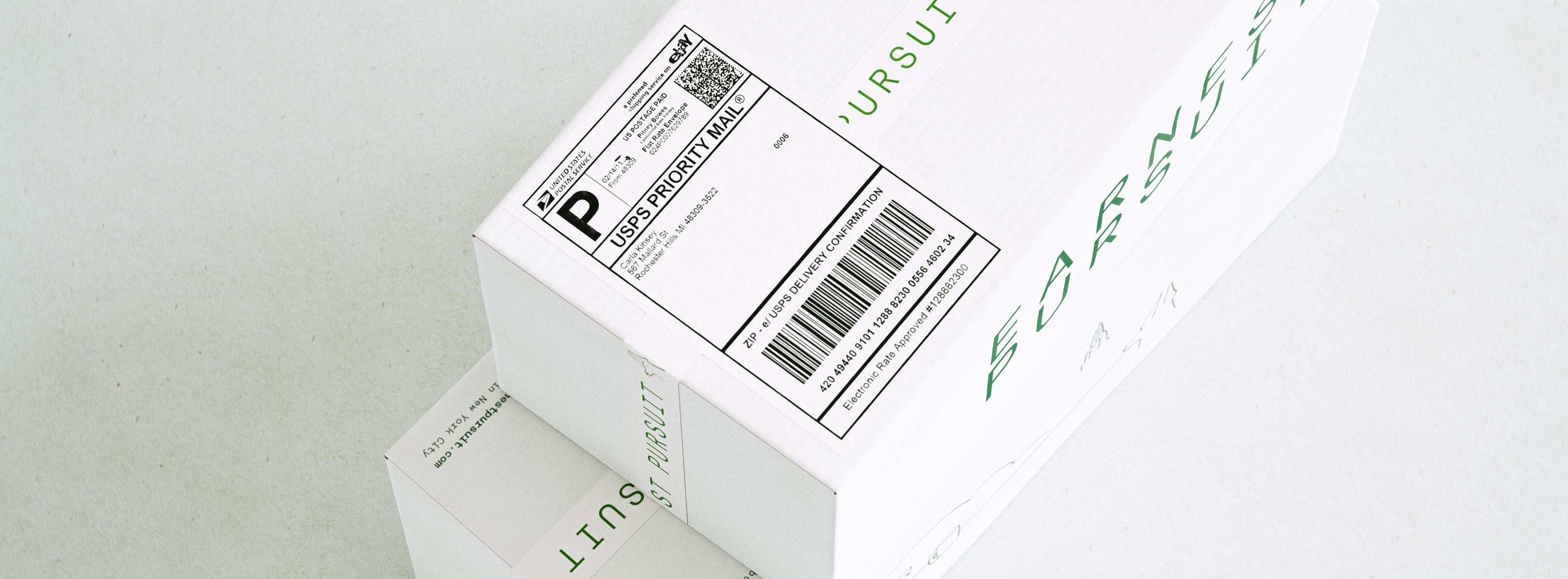 A tight, angled macro of a white shipping box focuses on its USPS Priority Mail label — the bold black "P" logo, printed sender block, delivery-confirmation barcode and rate-approved line — applied cleanly to the corrugated lid. Behind and around it, the forest-green EARNEST PURSUIT wordmark and the fine single-line skyline illustration wrap the box, with a second carton stacked beneath. The board is uncoated matte corrugate printed in one green ink, the shipping label integrated so it sits comfortably beside the brand graphics rather than fighting them. The image speaks to structural packaging design and print-ready artwork that accommodates real carrier labelling — the practical side of designing a shipping system for direct-to-consumer coffee.