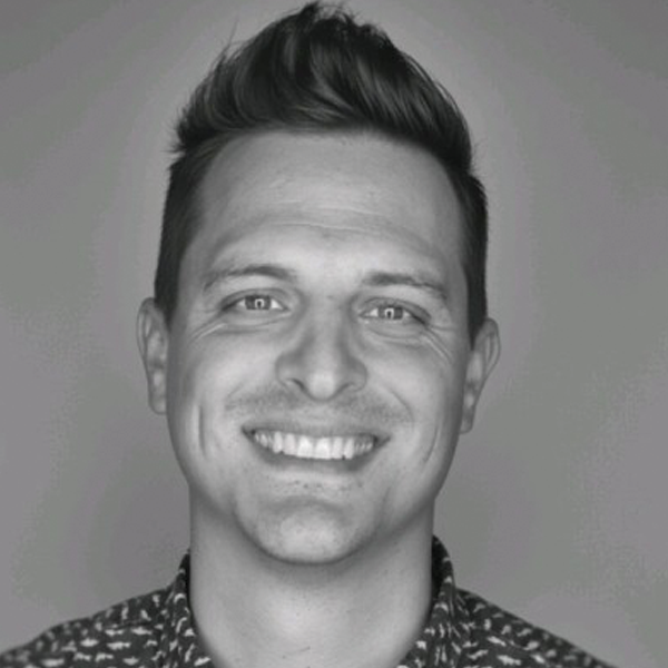 Smiling man with short dark hair styled upward wearing a patterned shirt against a plain background.