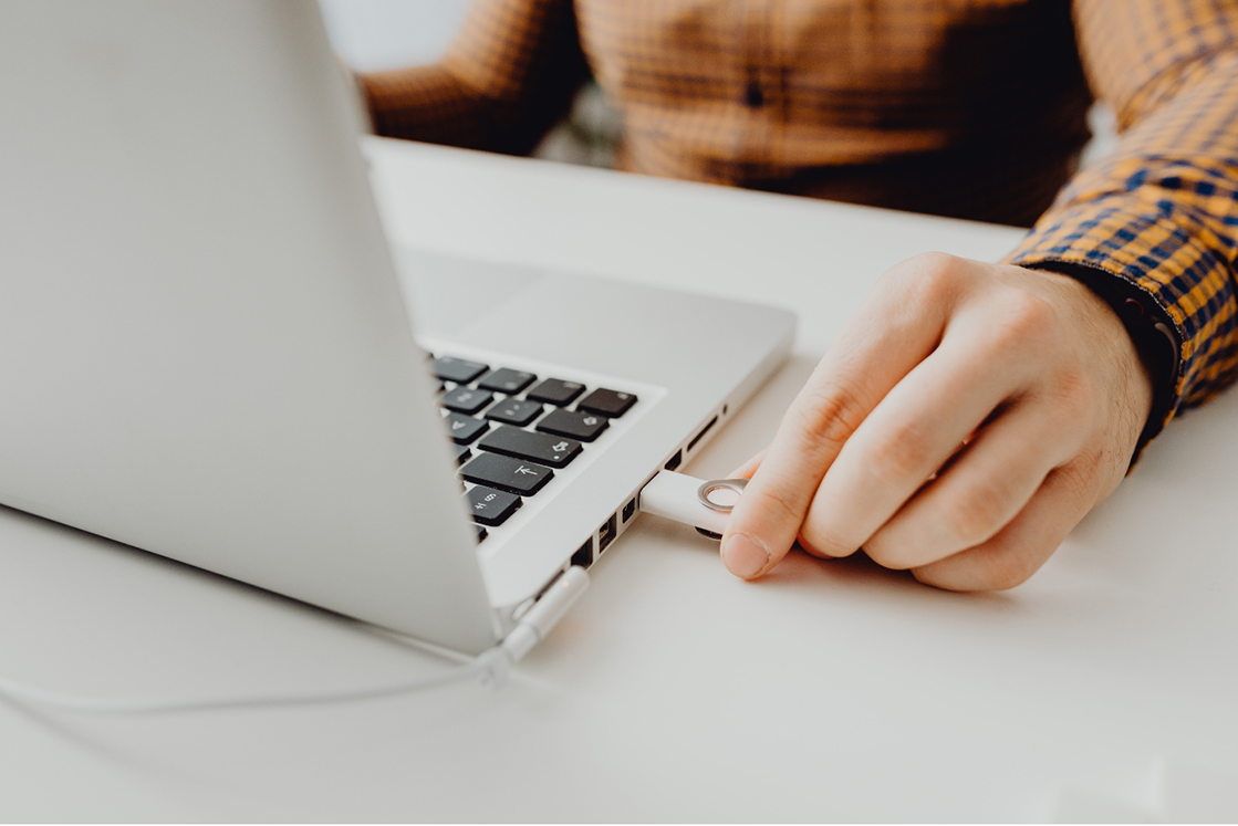Close-up of a person inserting a USB drive into a laptop, highlighting potential portable application security risks.