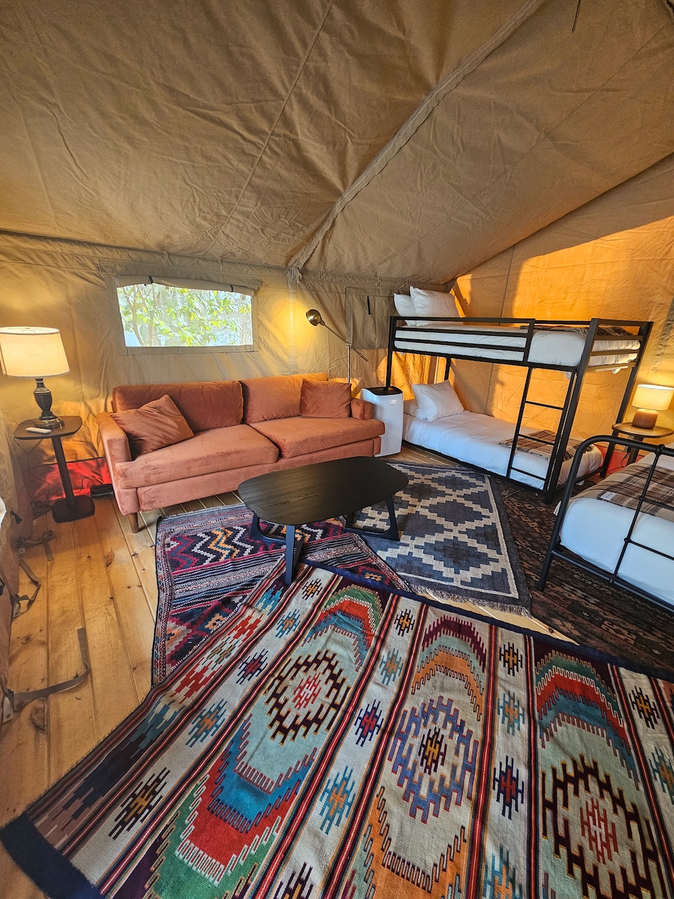 Wide interior shot of a Roamstead Safari Tent with colorful rugs, a sofa, and bunk beds.