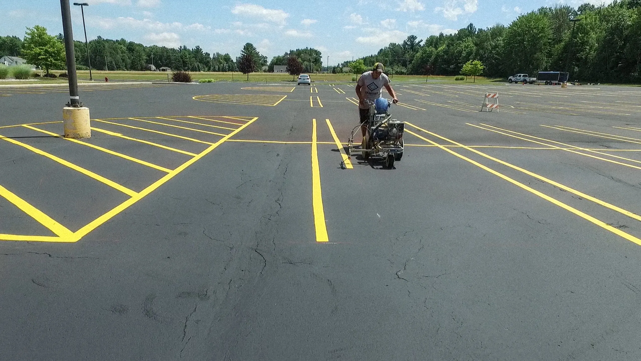 Worker painting yellow parking lot lines with striping machine