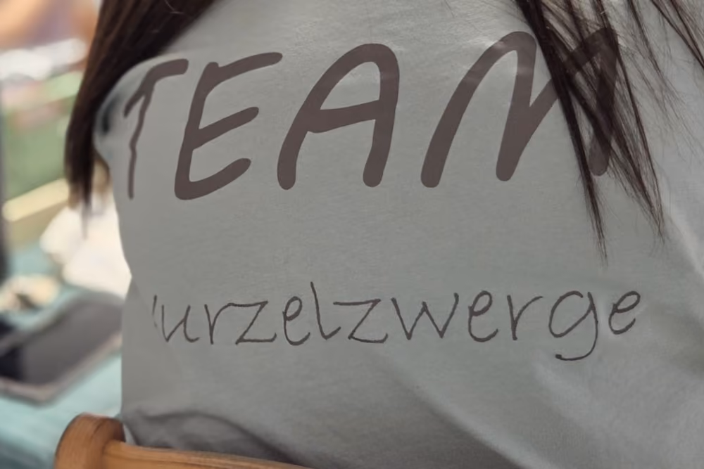T-Shirt mit der Aufschrift "TEAM Wurzelzwerge" in brauner Schrift auf grauem Stoff.