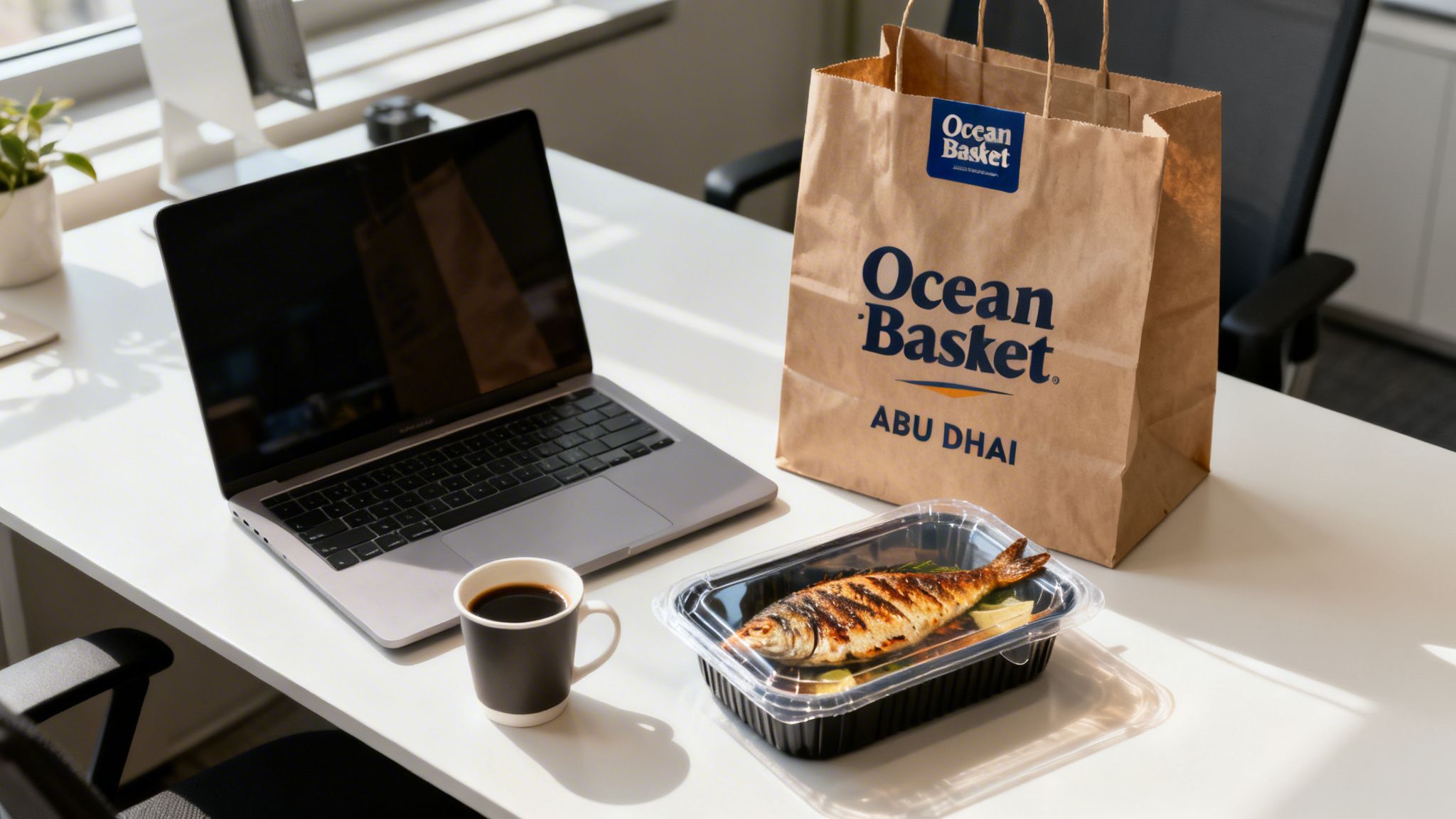 A takeaway grilled fish meal from Ocean Basket Abu Dhabi, coffee, and a laptop on a desk.