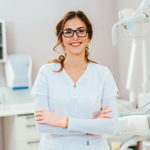 a smiling dentist standing in a treatment room with her arms crossed