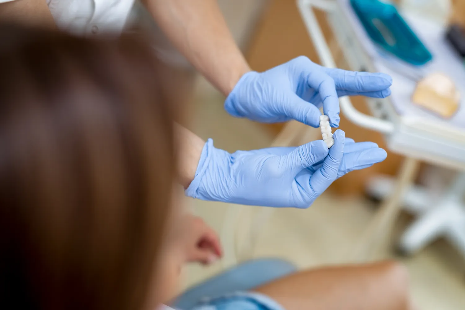 a dentist wearing blue gloves holding a dental bridge