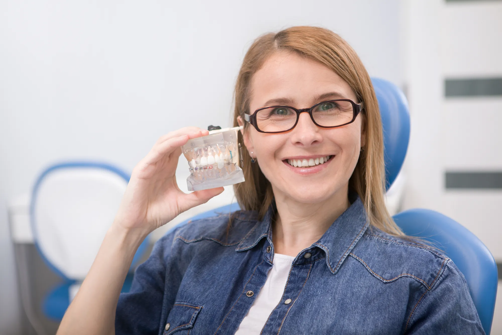 a woman wearing glasses holding a teeth model
