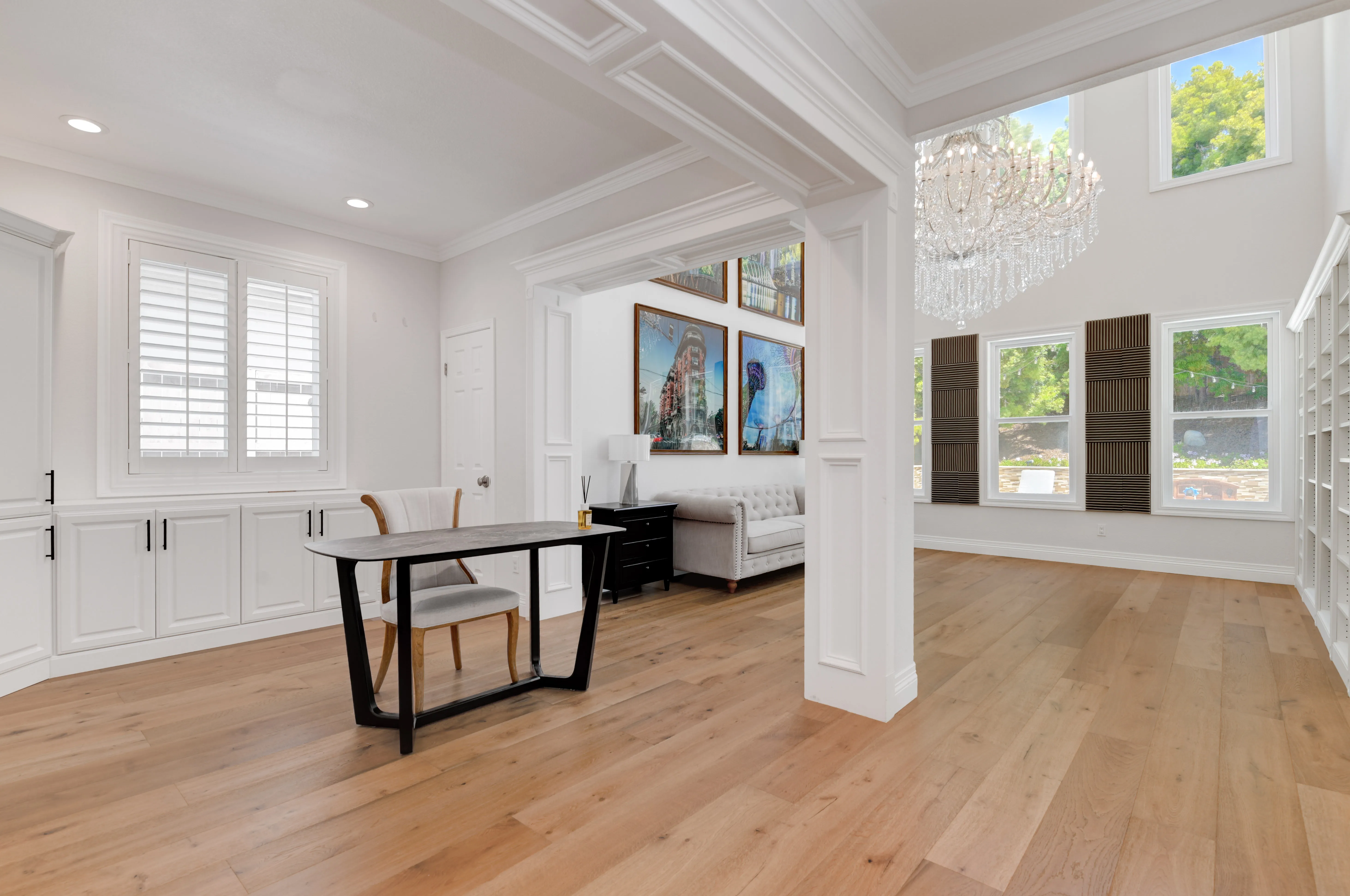 Open living area with custom wall panels, built-in cabinets, wide-plank wood floors and a two-story chandelier