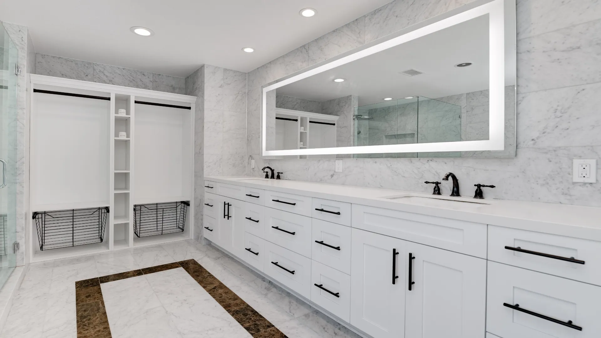 Primary bathroom with a long double vanity, lighted mirror and built-in closet shelves