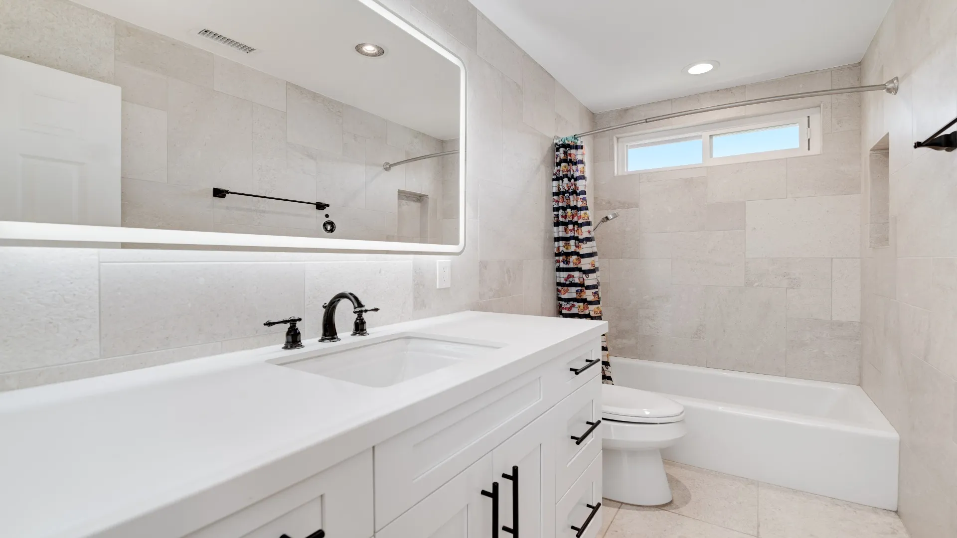 Bathroom with a white vanity, black fixtures, lighted mirror and tub-shower