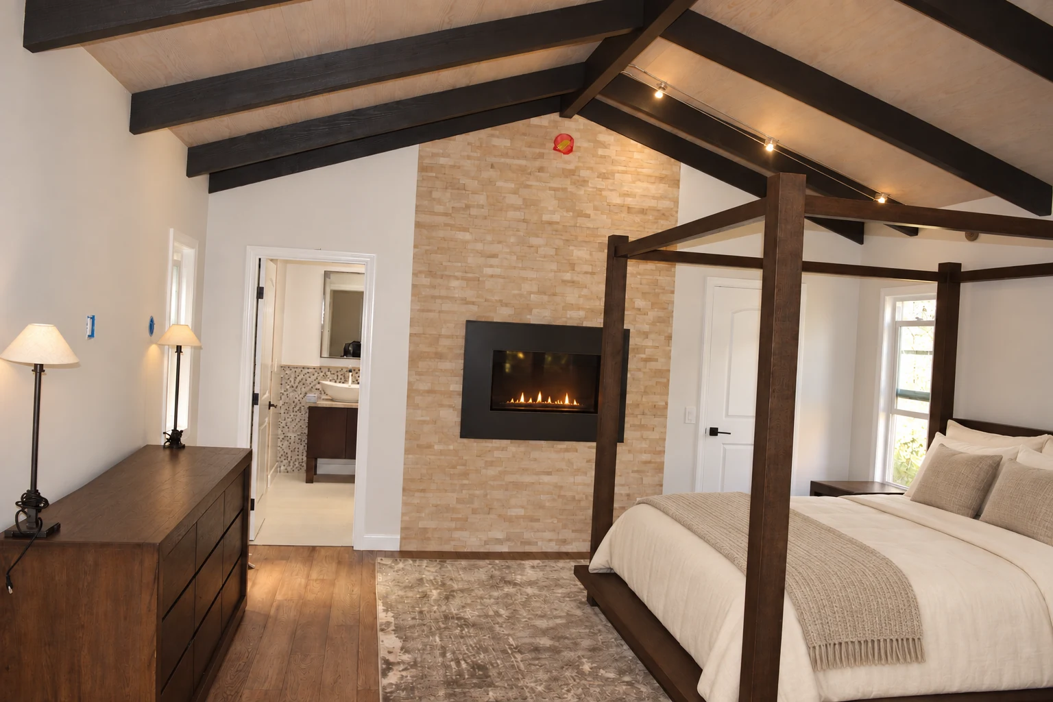 Finished bedroom interior with a beamed vaulted ceiling, wood floors and a stone fireplace wall
