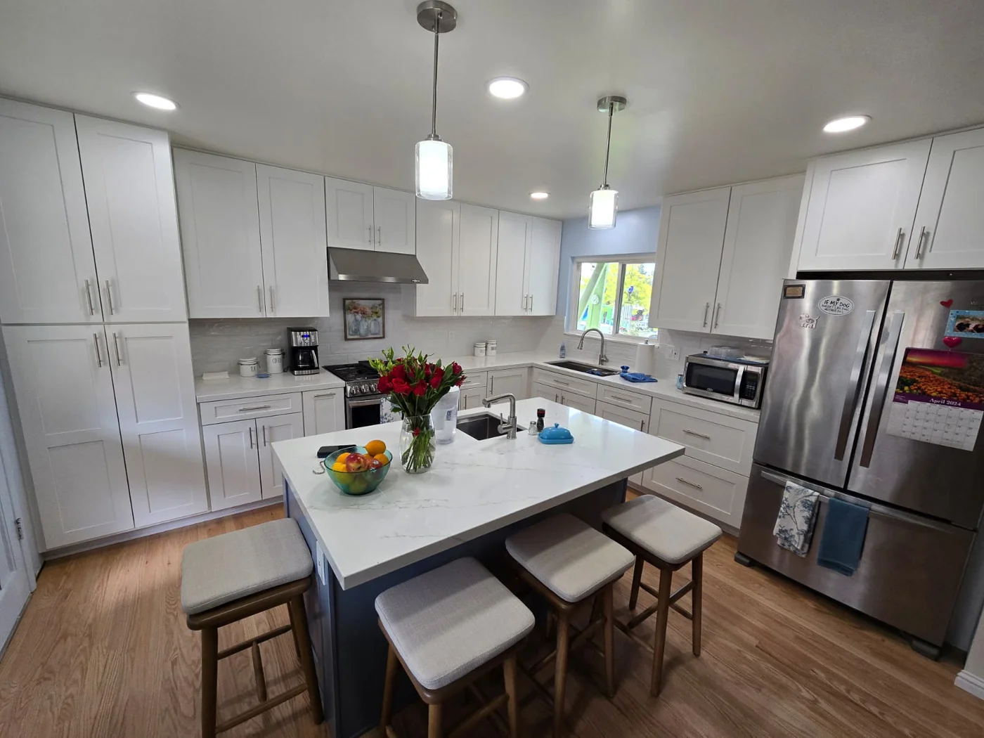 White kitchen with a dark island, seating and wood flooring