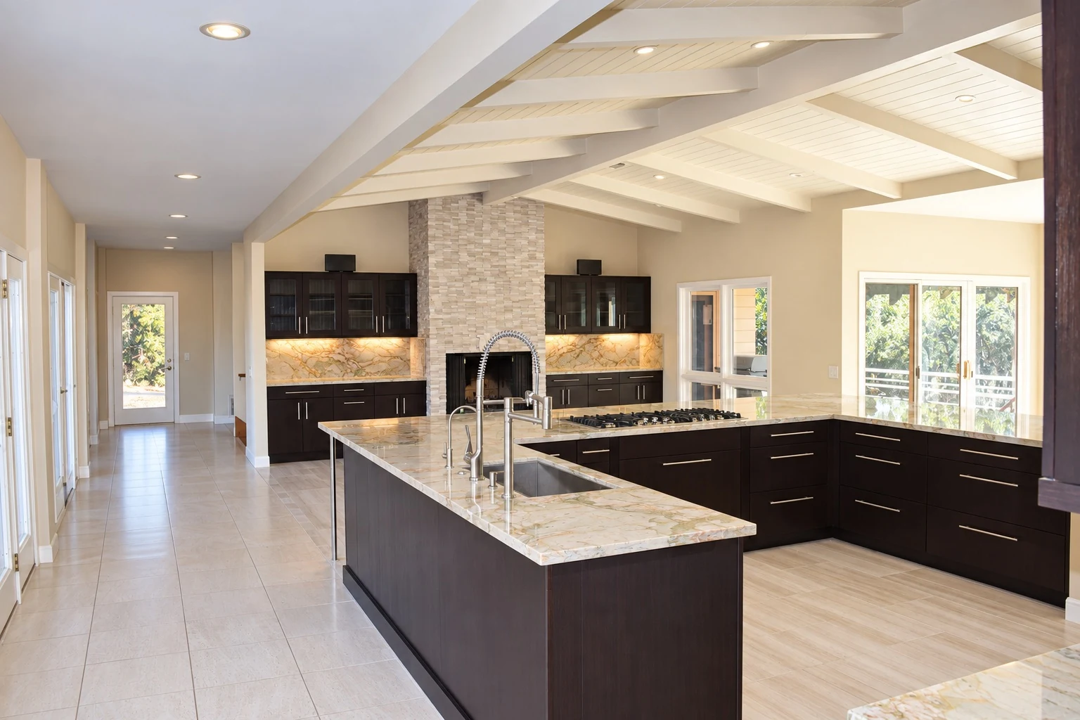 Custom kitchen with a large custom island, dark cabinets, stone counters and exposed ceiling beams