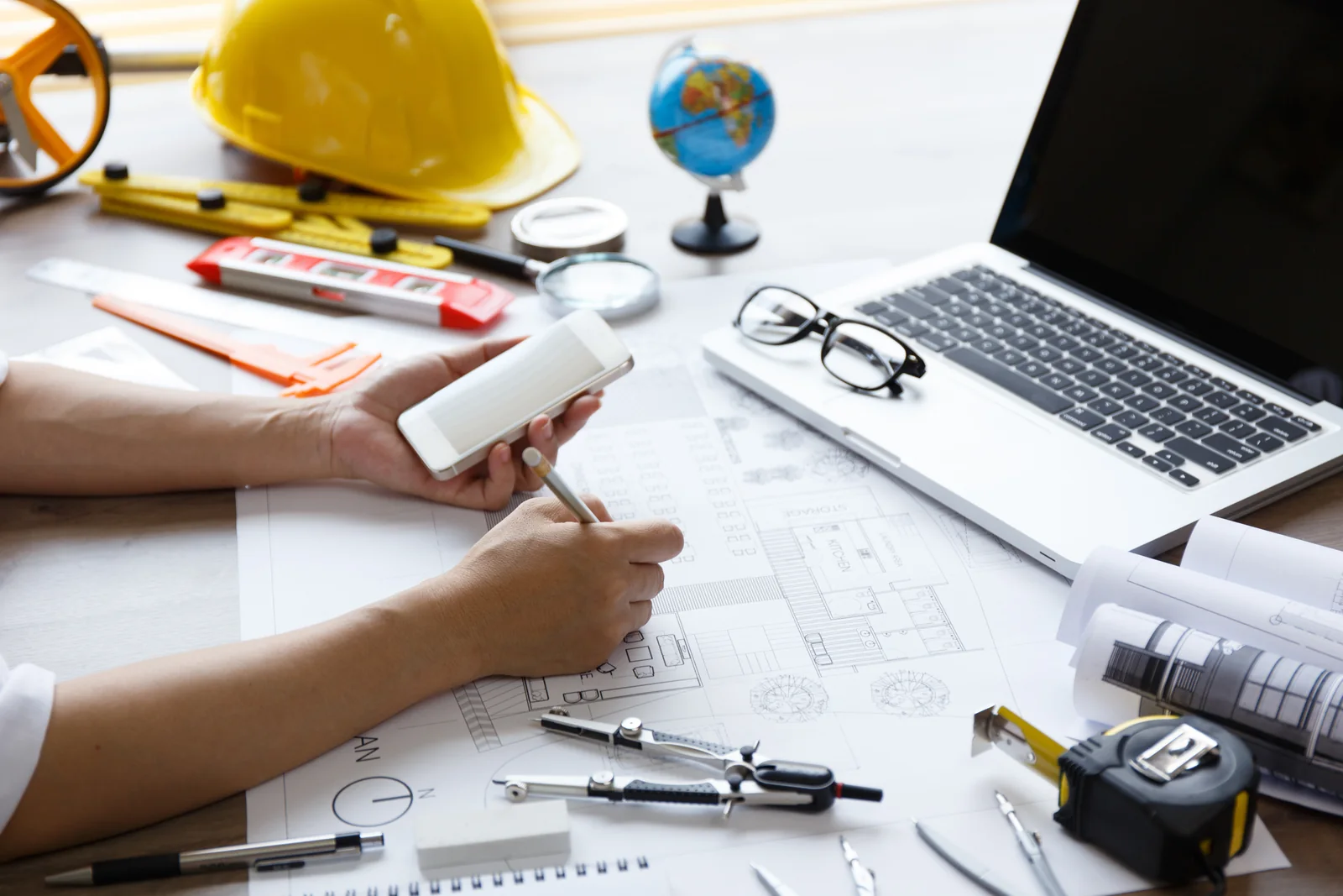 Desk with house plans, a hard hat and a laptop