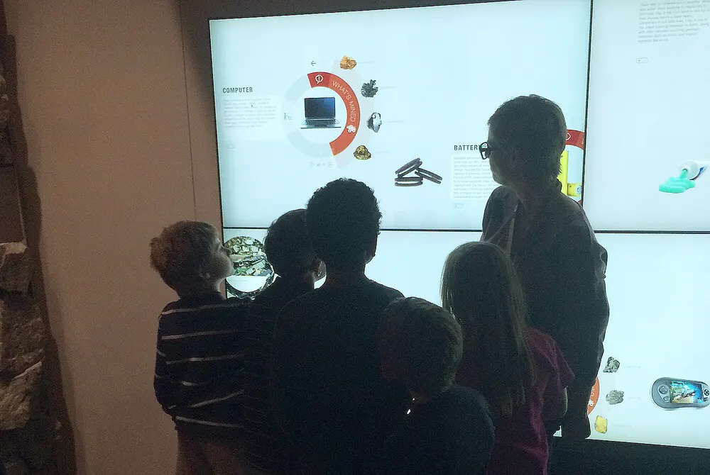 Group of visitors exploring minerals and everyday objects on an interactive museum touch wall