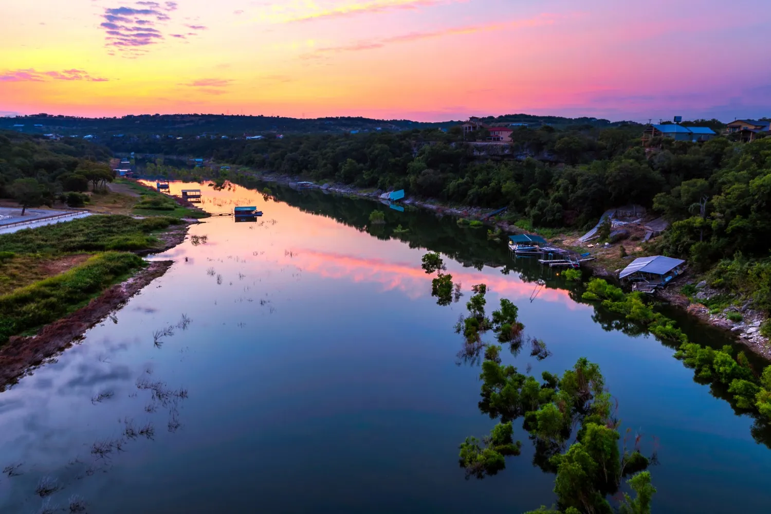 Dripping Springs water tower at sunset with vibrant skies, overlooking a highway and tree-covered hills.