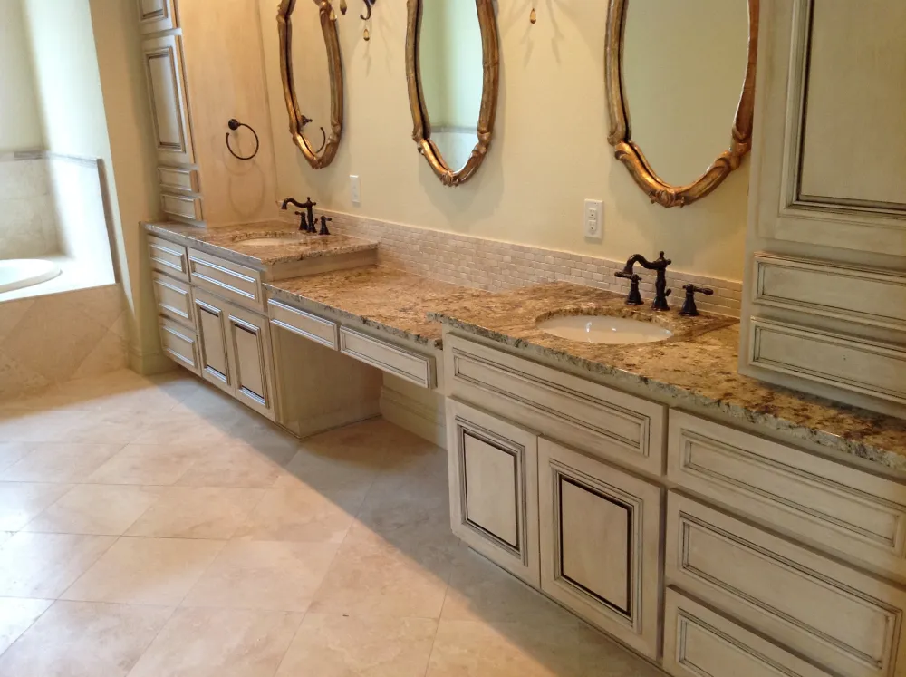 Elegant bathroom with double vanities, granite countertops, and antique-style mirrors above cream-colored cabinetry.