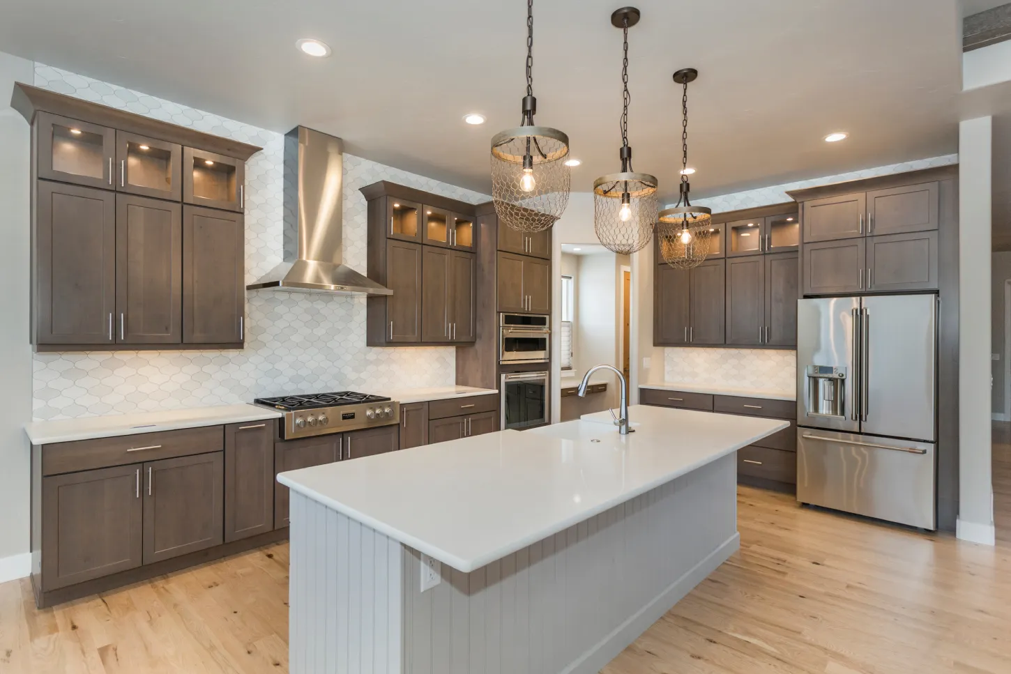 Contemporary kitchen with wooden cabinets, stainless steel appliances, white subway tile backsplash, a large white island countertop, and pendant lighting above the island.