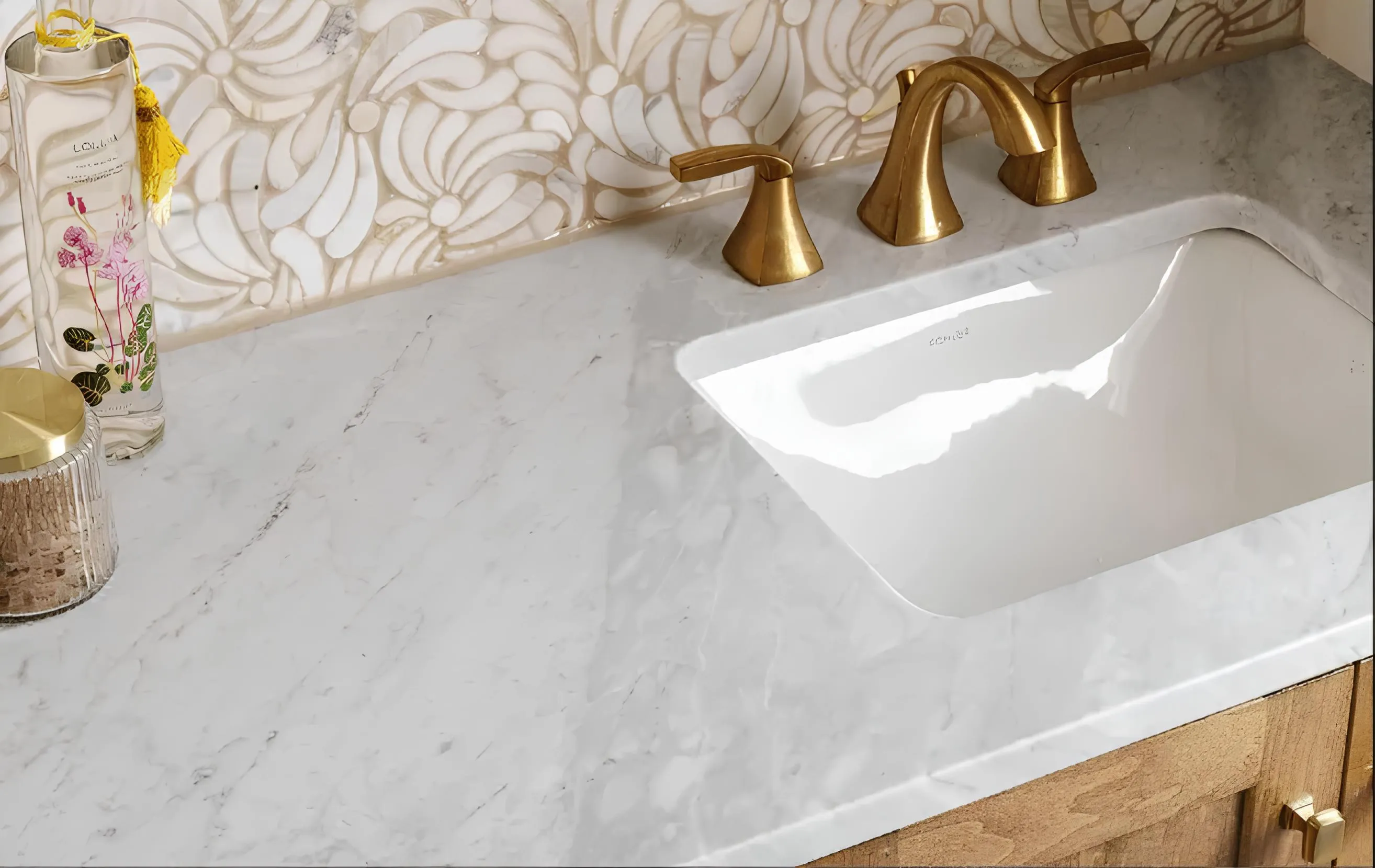 Elegant bathroom vanity with marble countertop, gold faucet, and floral mosaic backsplash.
