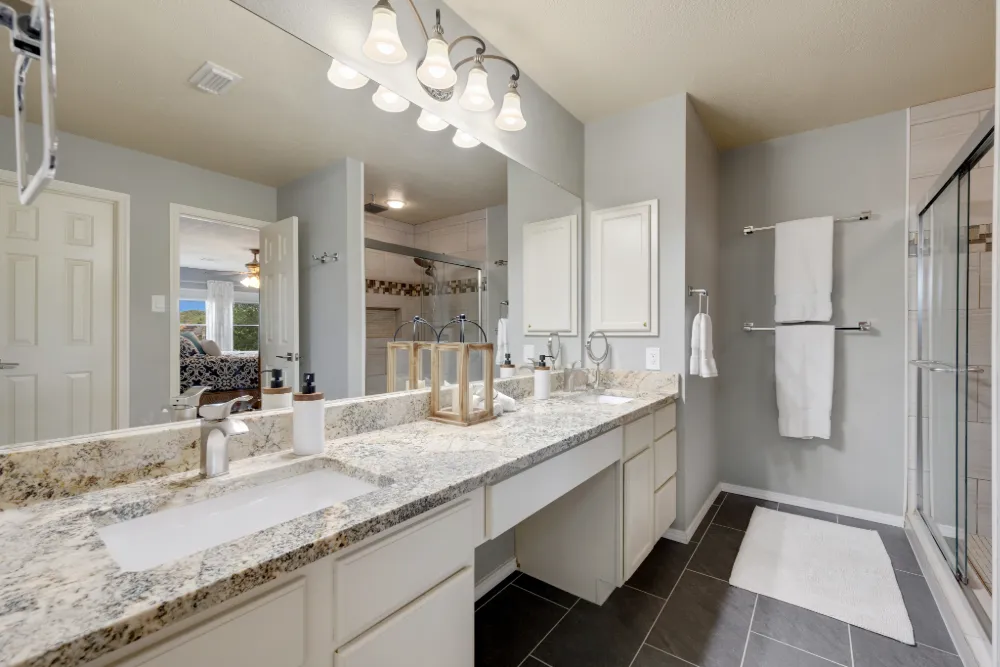 Modern bathroom with granite countertop, sink, large mirror, glass-enclosed shower, and white towels on towel racks.