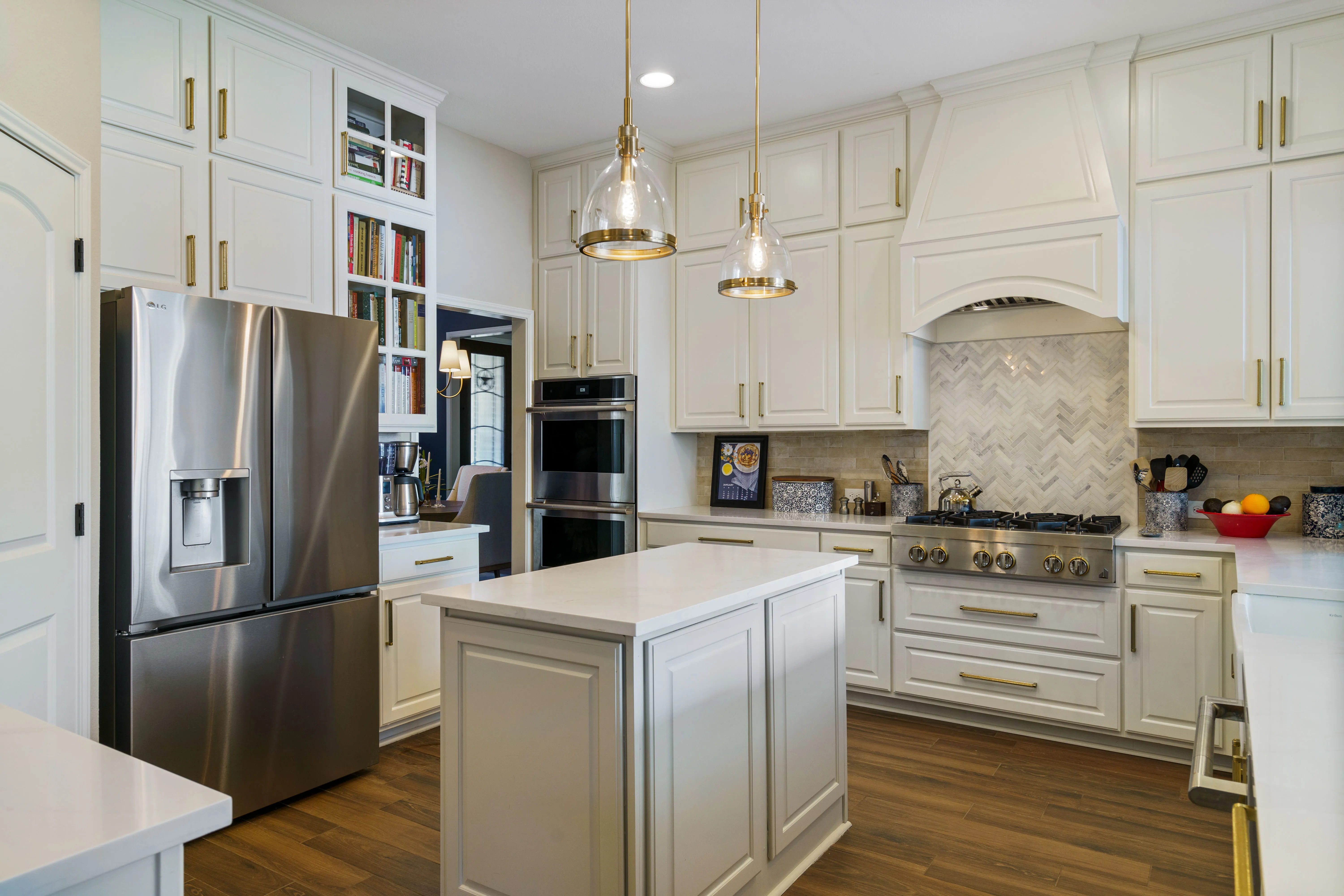 White kitchen with granite island, stainless steel appliances, and gold pendant lighting