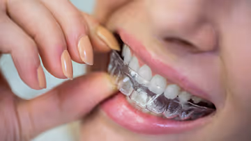 Close-up of a person holding a clear dental aligner near their teeth, demonstrating its use for teeth straightening.