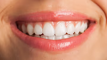 Close-up of a smiling person's mouth showing straight, white teeth and glossy pink lips.