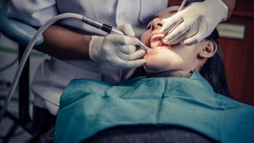 Dentist performing dental procedure on patient lying back in a chair, using dental instruments inside the patient's open mouth.