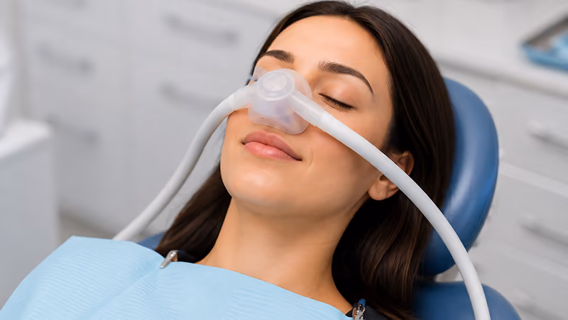 Young woman reclining in a dental chair with eyes closed, wearing a nasal sedation mask.
