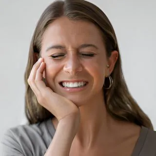Woman wincing and holding her cheek from tooth pain