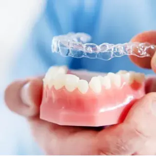Hand holding a clear aligner above a model of lower teeth
