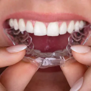Hands holding a clear aligner in front of a bright smile