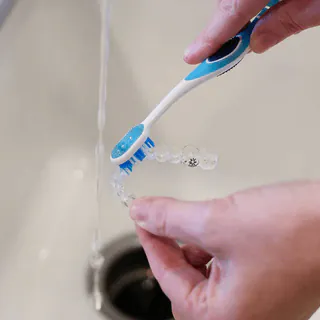 Cleaning a clear aligner with a toothbrush under running water