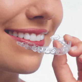 Woman holding a clear aligner beside her smile
