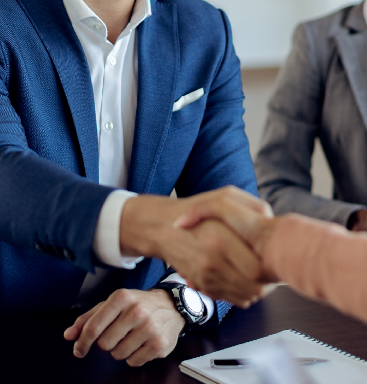 Two business professionals shaking hands across a table during a meeting, symbolising partnership and collaboration.