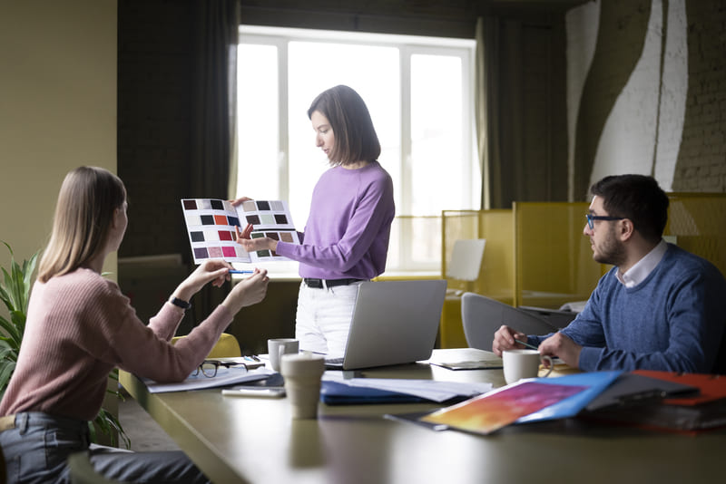 Equipo de marketing colaborando en estrategia de marca con muestras de color, materiales creativos y conceptos de diseño durante una reunión empresarial Hiweb